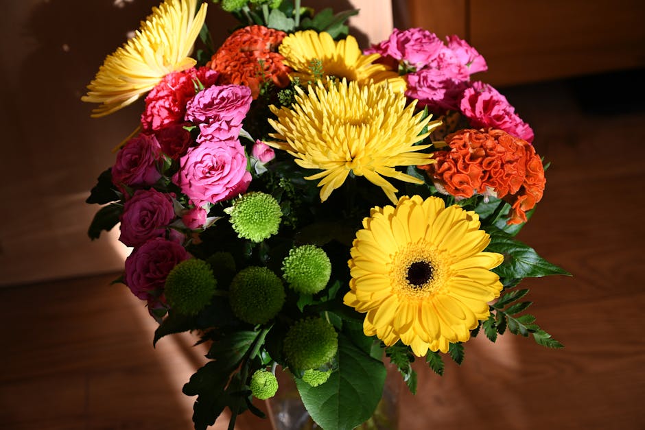 A vibrant floral arrangement featuring large yellow gerbera daisies with dark central discs, bright pink spray roses with multiple small petals, bold orange carnations with ruffled petals, and small g