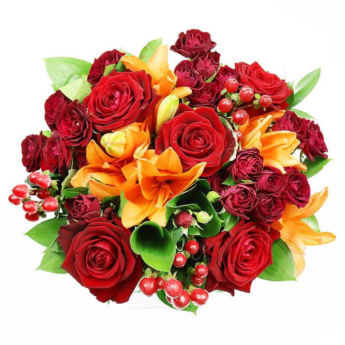 Presented head-on from above on a flawless white field, this densely arranged circular bouquet presents a rich interplay of colour, scent and surface. Large, deeply hued red roses dominate the picture, their velour-like petals unfurling to form layered, intimate centres that read as timeless symbols of love. Complementing these are bright orange Asiatic lilies, their broad trumpets and visible stamens introducing vivid contrast and sculptural line; a few lilies remain in tighter buds, creating a sense of progression as if the bouquet might subtly change over the day. Interspersed among them are compact spray roses in a wine or burgundy tone, small but sumptuous, offering a velvet-like texture and deepening the tonal range. Small clusters of glossy red Hypericum berries provide punctuated highlights-gleaming, spherical accents that invite the eye to travel across the arrangement-while ample glossy green foliage (suggestive of salal or ruscus) lifts and frames the blooms, giving them breathing room and lively freshness. The lighting is gentle and even, revealing every petal edge and berry sheen without harsh shadows, so the composition feels both opulent and impeccably neat. This bouquet reads as an eloquent gift for romantic milestones, a warm housewarming centrepiece, or an elegant thank-you, and it carries the quiet confidence of a local florist's hand. I picture it brightening a mantel in a Camberley townhouse or arriving as a celebration bouquet for friends who have just moved in near the Theatre or the town centre, its colours echoing late-summer evenings and the welcoming warmth of home.
