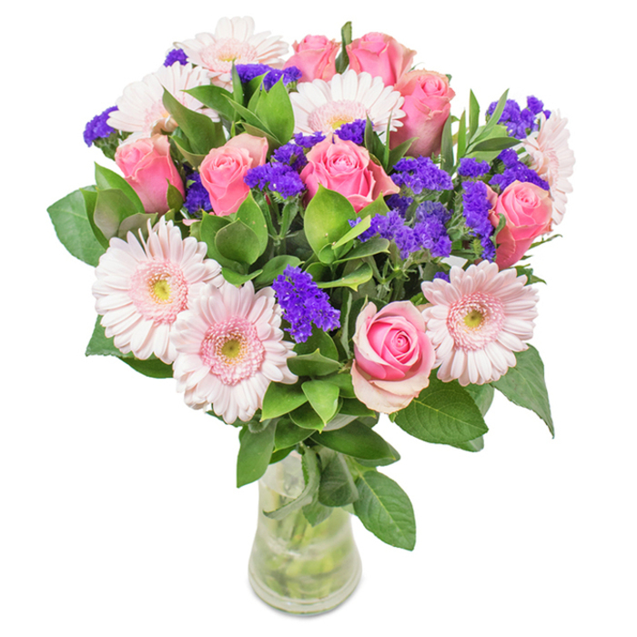 This Camberley-inspired floral bouquet, arranged with artistry and expertise, is presented in a classic clear glass vase and set against a pristine, soft-white background. At its centre, a harmonious union of seven to nine medium pink roses-many just on the verge of blooming-showcases spiraled petals and a gentle gradient from blush to deeper rose. Interlaced with these are five to seven pale pink gerbera daisies, easily recognized by their large, round heads and elegant rays of petals, each bloom glowing softly as if kissed by sunlight streaming through a window in the town's centre. Throughout the bouquet, clusters of vivid purple statice serve as striking accents, providing rich texture and a playful pop of depth that nods to the vibrant local gardens around Camberley. Deep green foliage encloses the arrangement, grounding its exuberance and heightening the sense of freshness, much like a walk through the town's serene parks. The clear vase allows clean lines and fresh-cut stems to be admired, hinting at the bouquet's recent handcrafting. This versatile arrangement, evocative of local joy and affection, suits celebrations from birthdays to anniversaries, Mother's Day tributes, or simply brightening up a Camberley workspace. The careful blend of roses, gerberas, statice, and greenery encapsulates the essence of community, celebration, and heartfelt beauty.